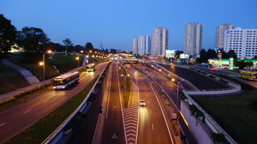 Ulica dużego miasta o zmierzchu, w tle widoczne są wysokie budynki wielorodzinne