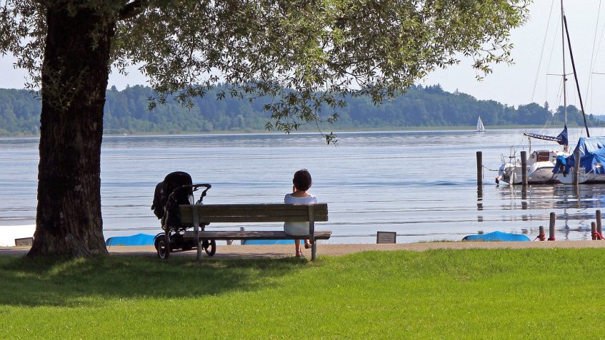 Kobieta z wózkiem siedząca na ławce nad jeziorem