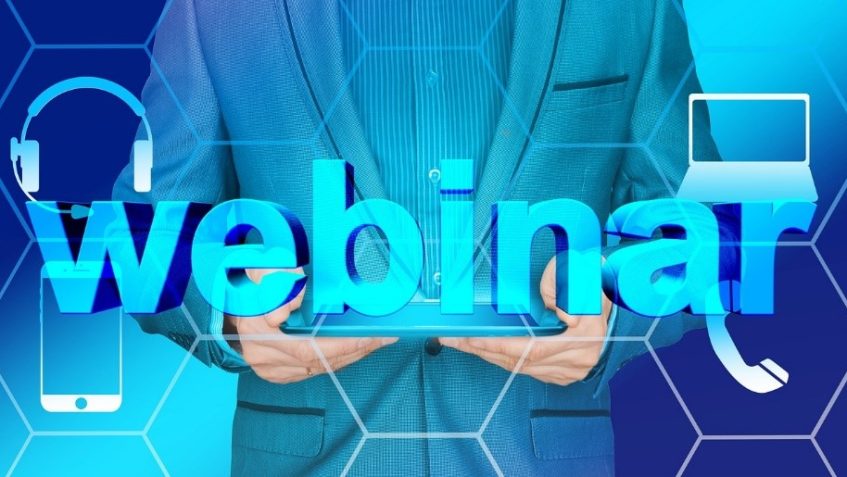 napis webinar, za nim człowiek trzymający tablet